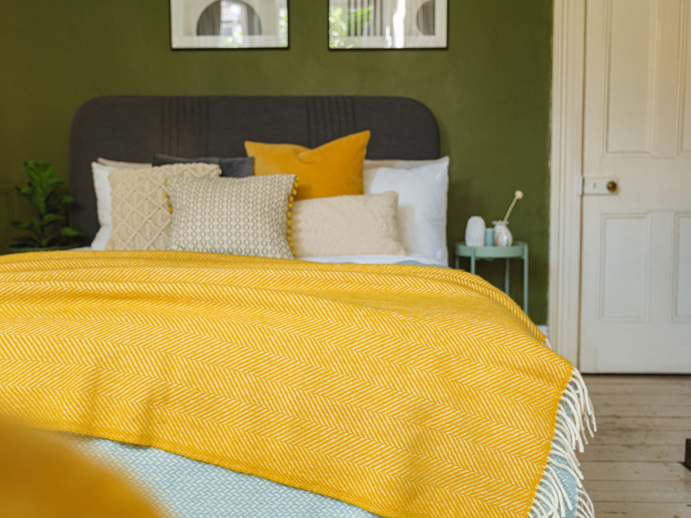 An extra large yellow herringbone wool blanket draped across a bed with yellow cushions