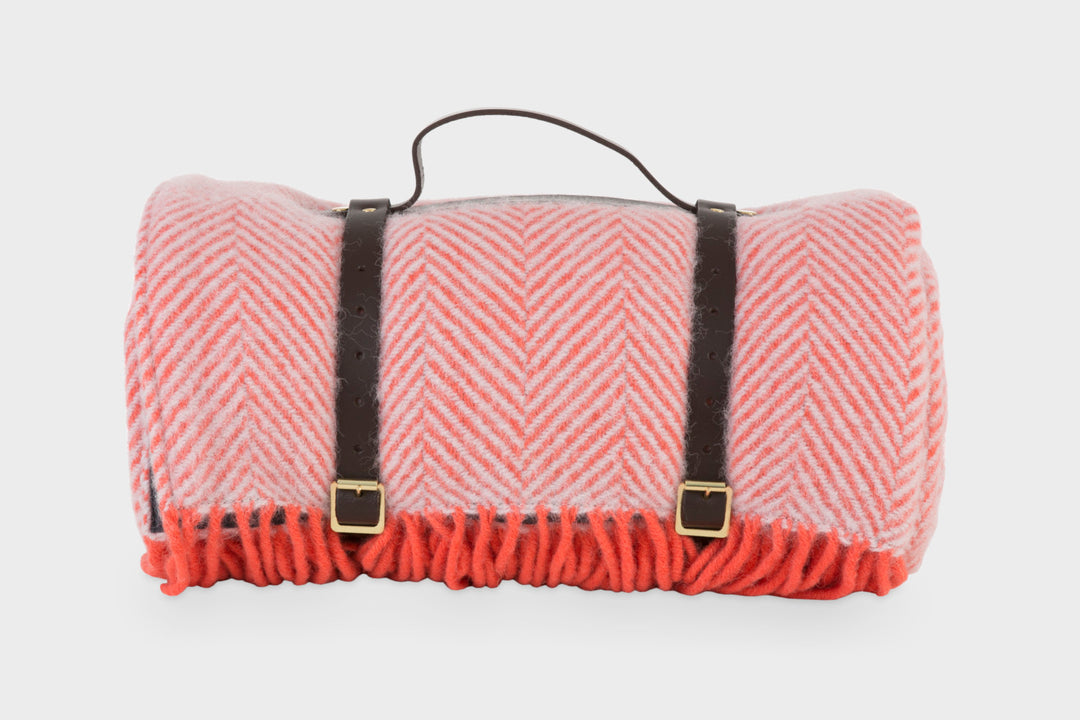 Pink wool picnic rug by The British Blanket Company rolled up with leather straps.