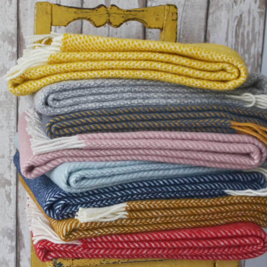 A pile of wool blankets from The British Blanket Company on top of a yellow velvet couch 