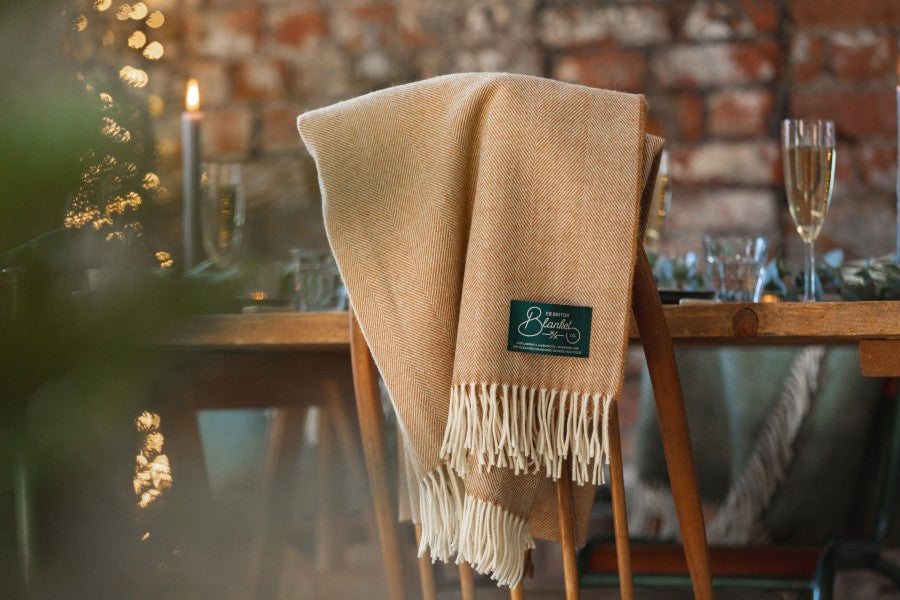 Warm beige wool blanket draped over a chair at a festive dining table with exposed brick. 