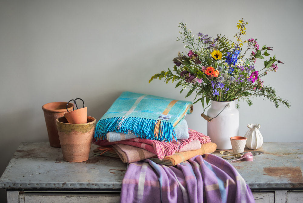 Garden flowers merino wool throw blanket collection stacked up with a rustic vase of flowers and terracotta flower pots by The British Blanket Company online shop