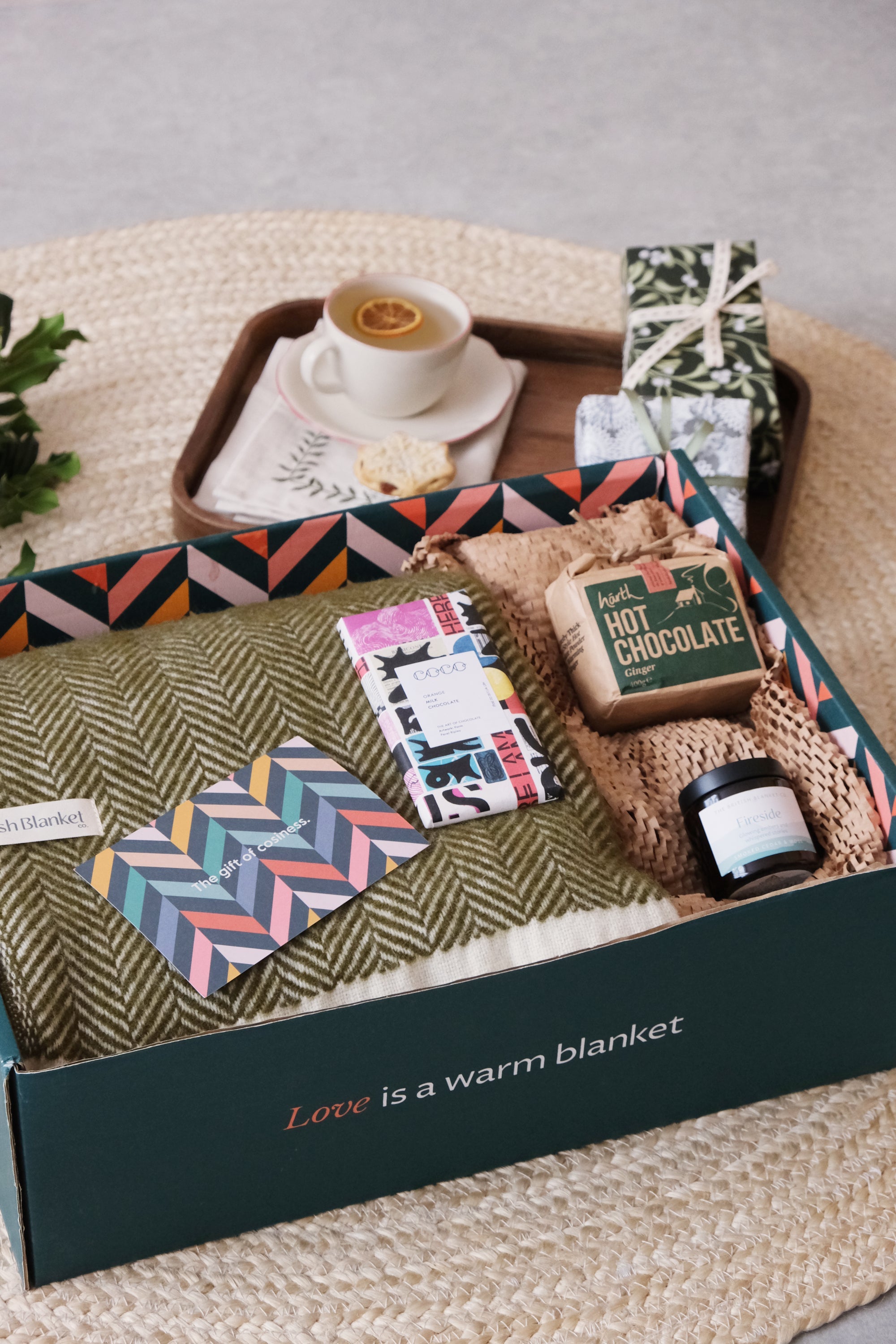 A hand holds a card above a box containing a jar of cream, socks, a book, and a jar of jam.