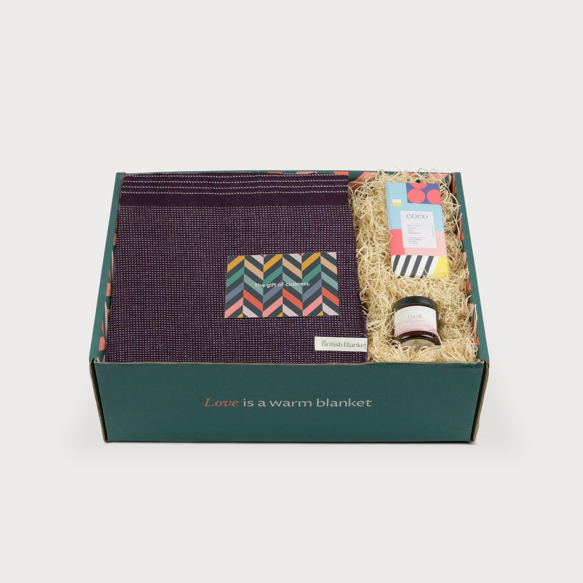 Alpaca Blanket Gift Box: Berry Purple, featuring a folded alpaca blanket, an amber jar candle, a sea salt chocolate bar, and a cozy-themed gift card in straw packing.