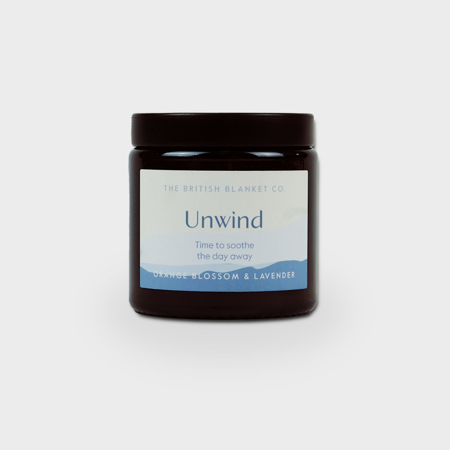 Amber jar candle labeled Unwind with orange blossom and lavender scent, part of the Alpaca Blanket Gift Box: Berry Purple from The British Blanket Co.