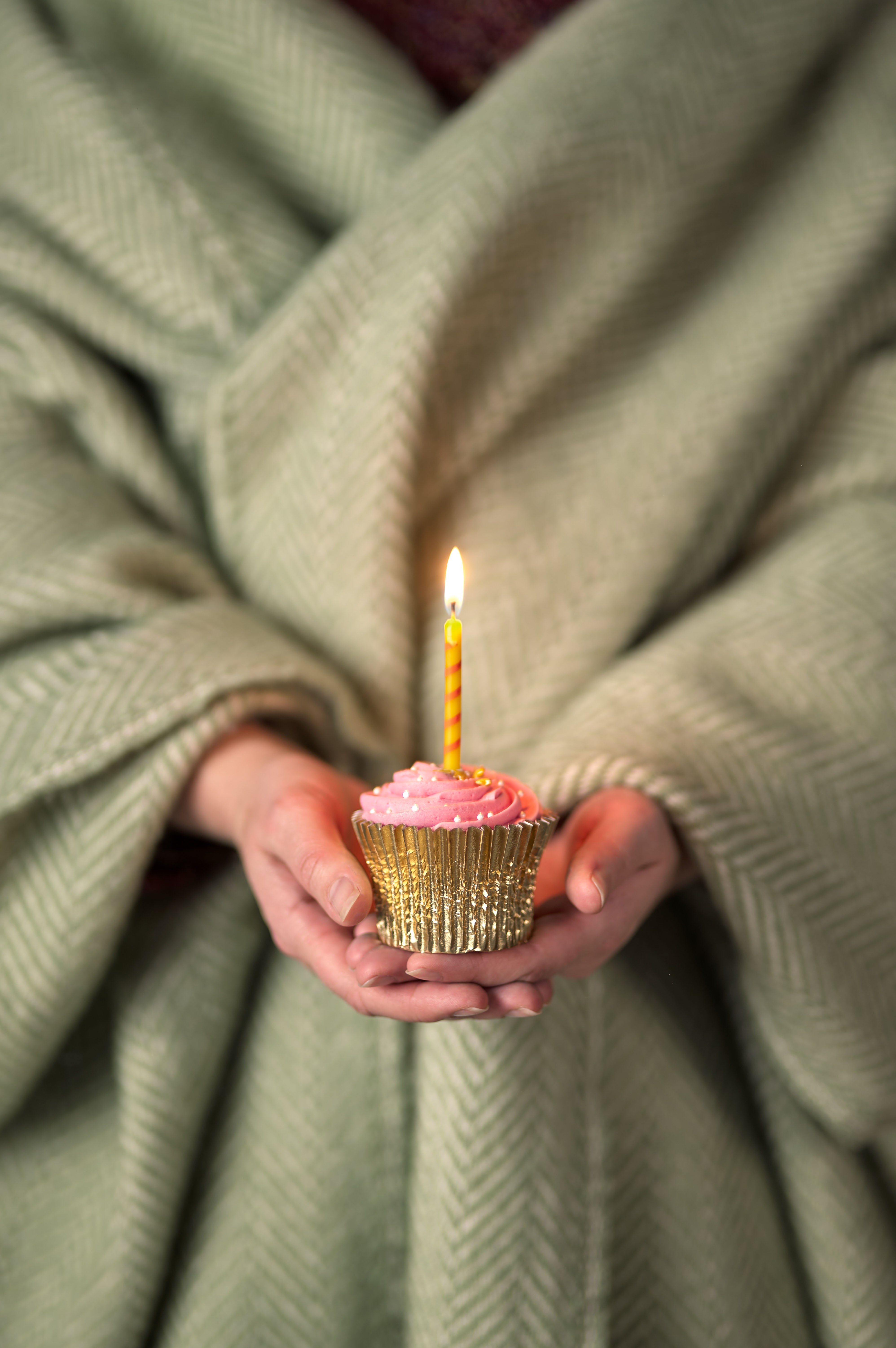 Hands holding a cupcake with pink frosting and a candle, symbolizing celebration. Ideal for gifting with a British Blanket Company Digital Gift Card.