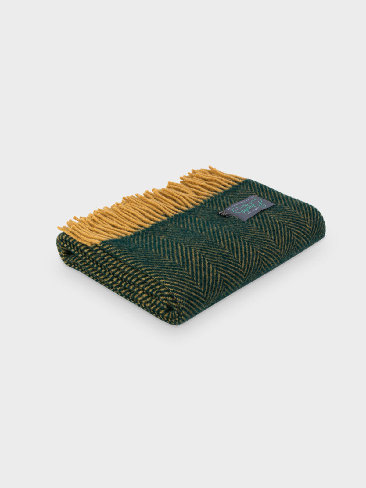 A folded green and mustard herringbone wool throw by The British Blanket Company.