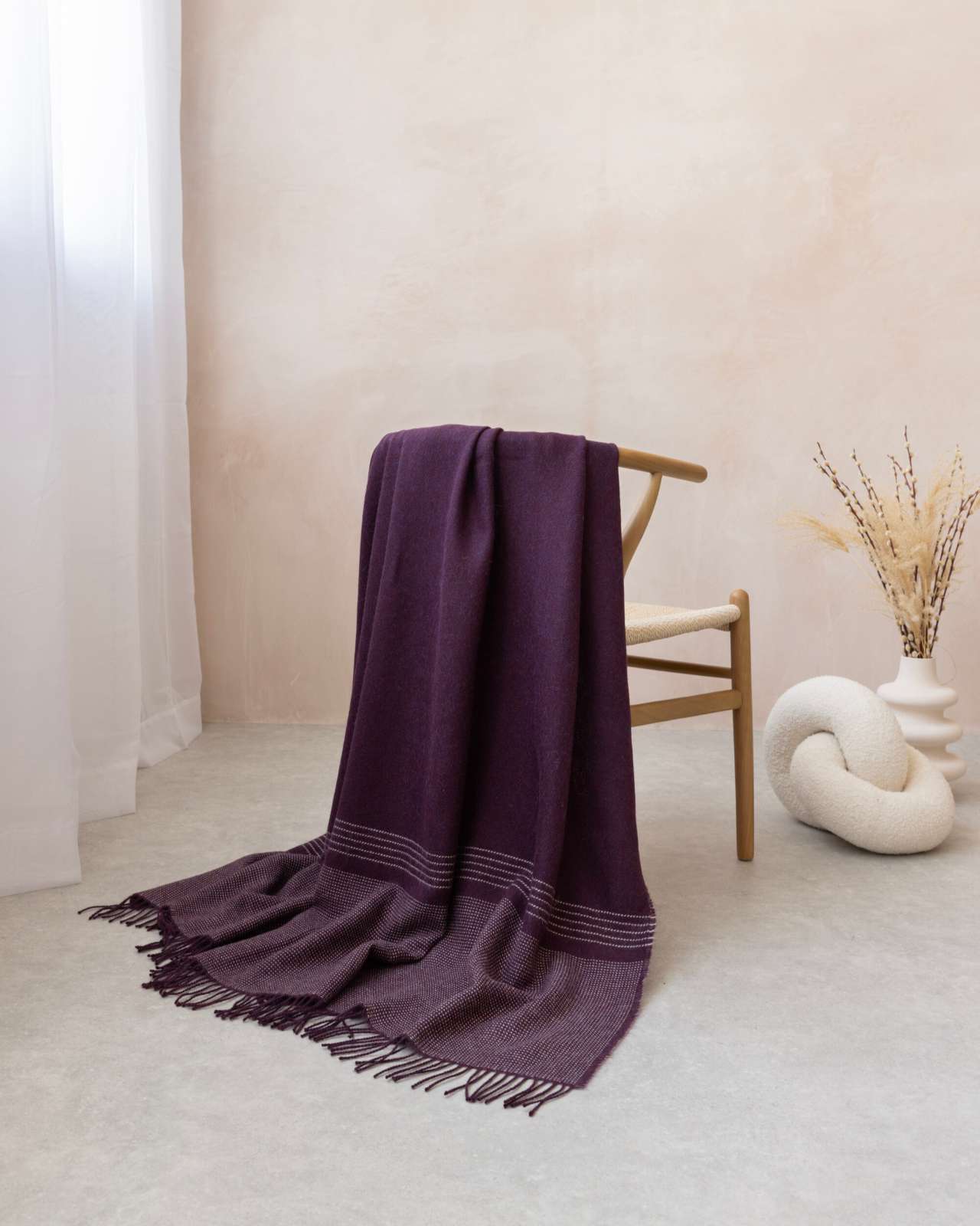 Alpaca Blanket Gift Box: Berry Purple, featuring a woven seat chair with plum throw, knot cushion, and vase with pampas, in soft natural light.