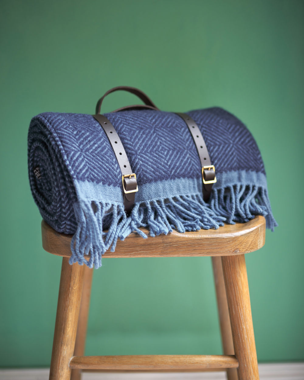Blue wool picnic blanket with leather straps on stool from The British Blanket Company