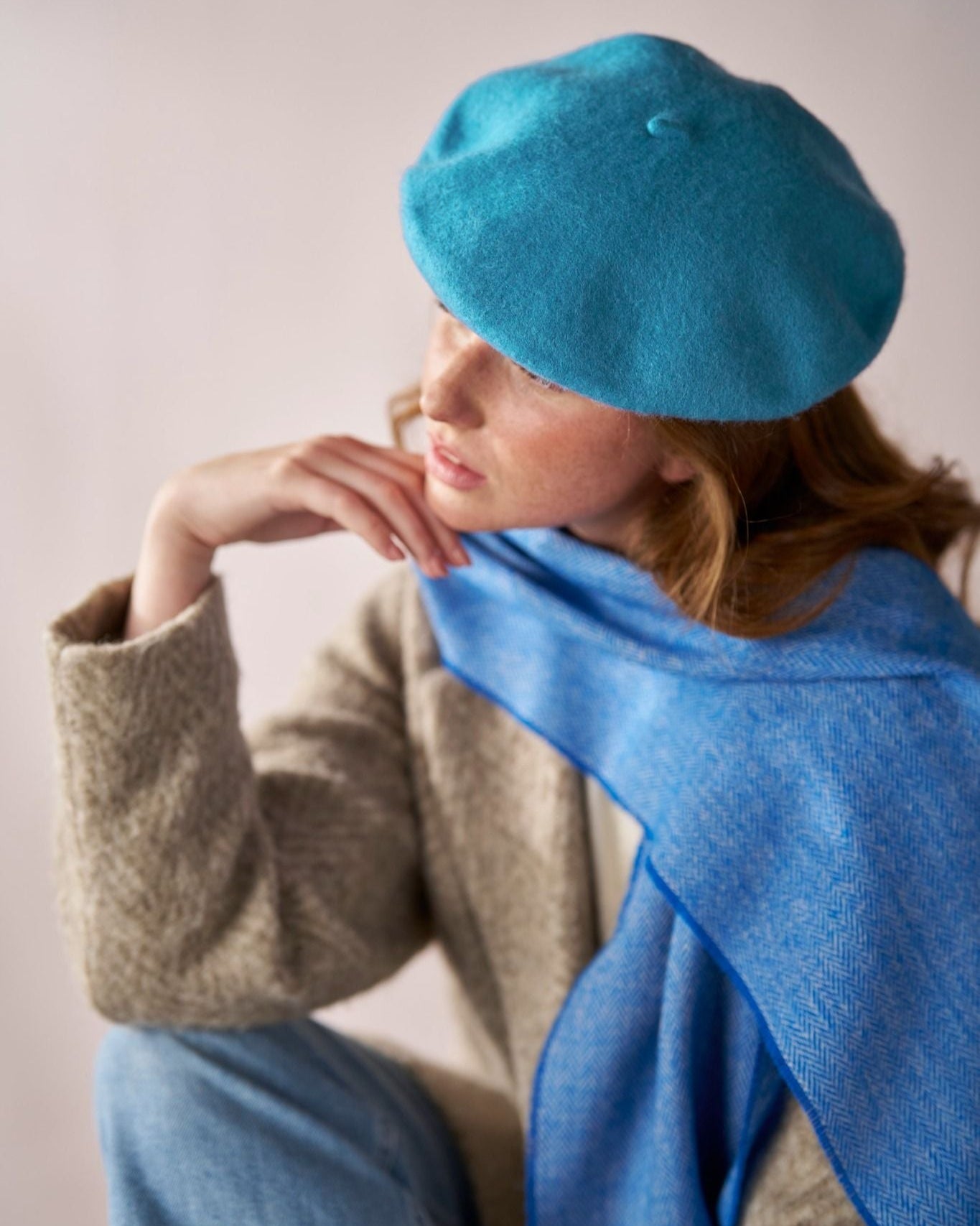 Young woman wearing the Wool Beret Hat: Teal Blue, showcasing its premium wool and elegant shape, paired with a light-blue scarf and neutral-tone coat.
