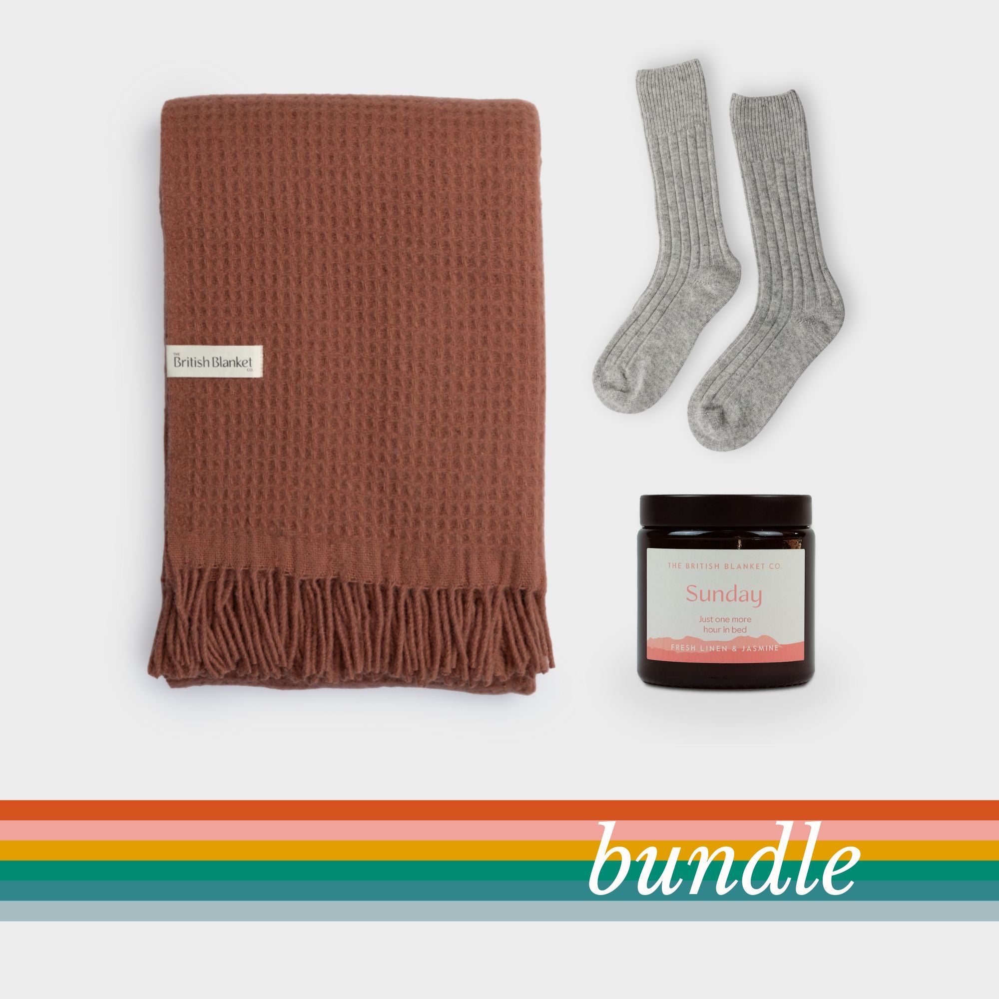Bright Friday Blanket Bundle: Brunswick featuring a folded rust-brown waffle throw, light grey rib-knit socks, and amber candle, all arranged on a plain backdrop.