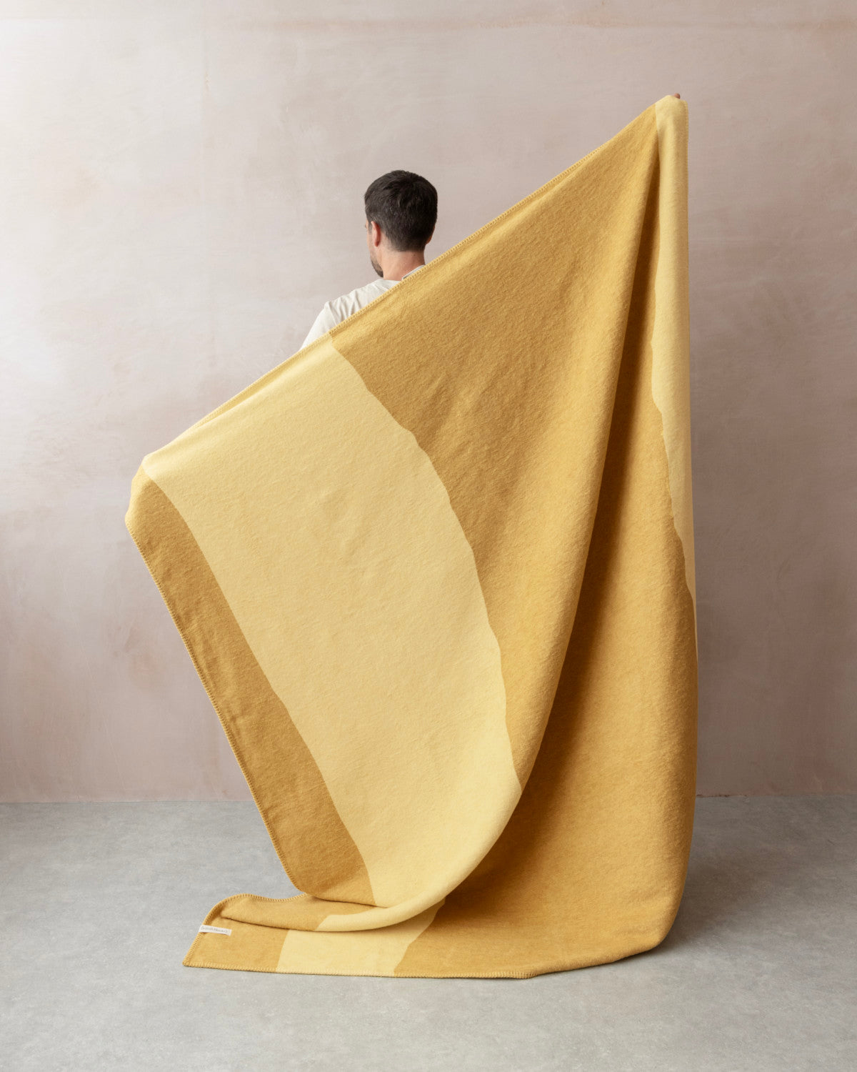 Person holding Cloud Cotton Blanket: Tide in Butter, showcasing its two-tone yellow stripes and soft, brushed finish, in a neutral-toned room.
