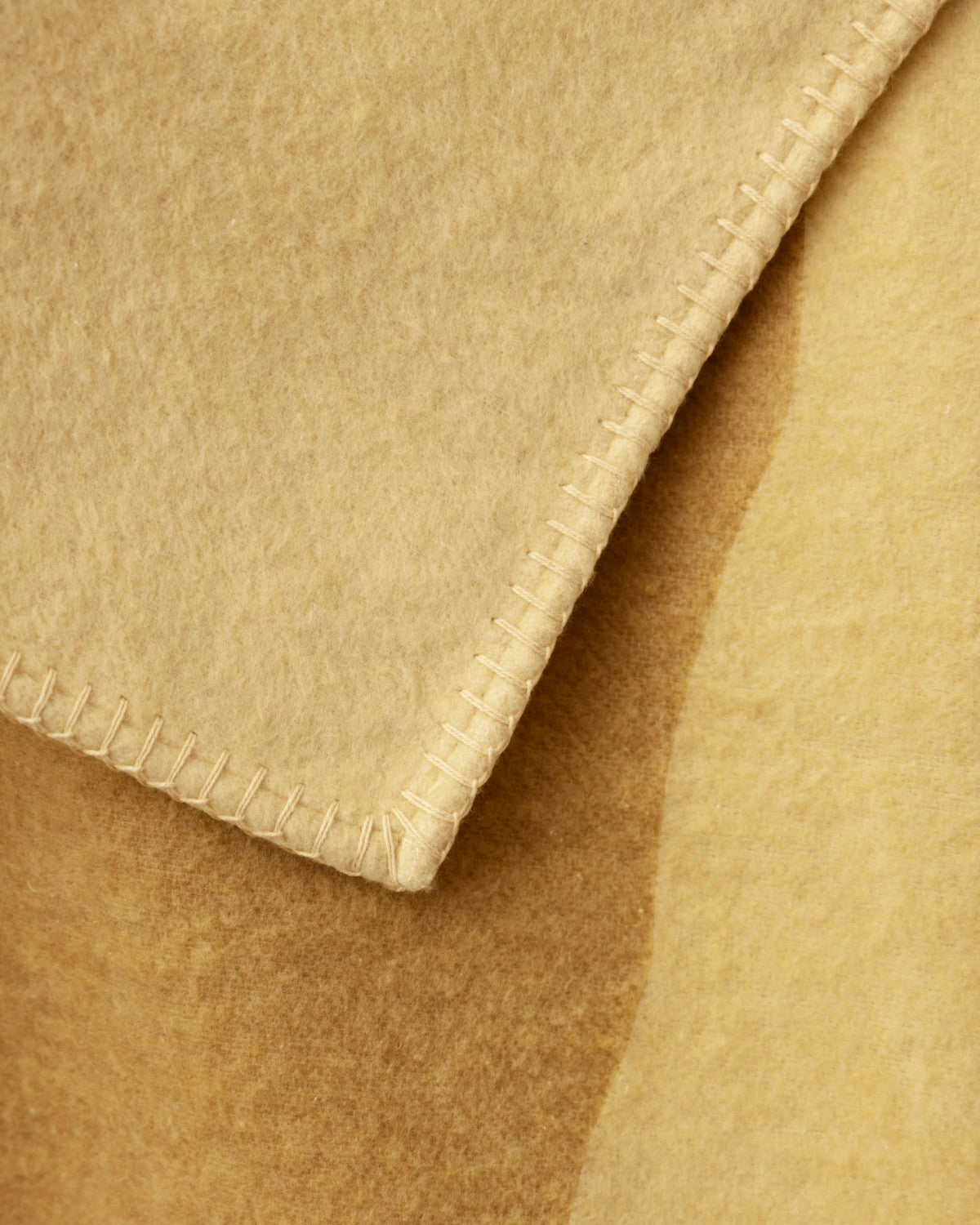 Cloud Cotton Blanket: Tide in Butter, showcasing a close-up of its soft, variegated texture, warm beige tones, and neat whip-stitched edges.