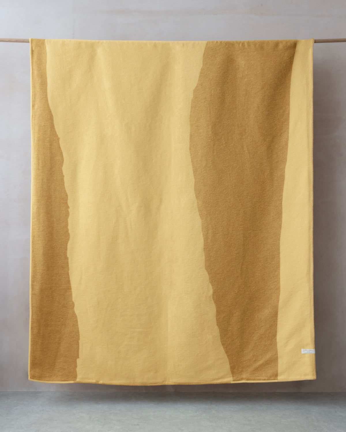 The Cloud Cotton Blanket: Tide in Butter, features a two-tone yellow design with a soft, brushed finish, draped over a wooden rod.