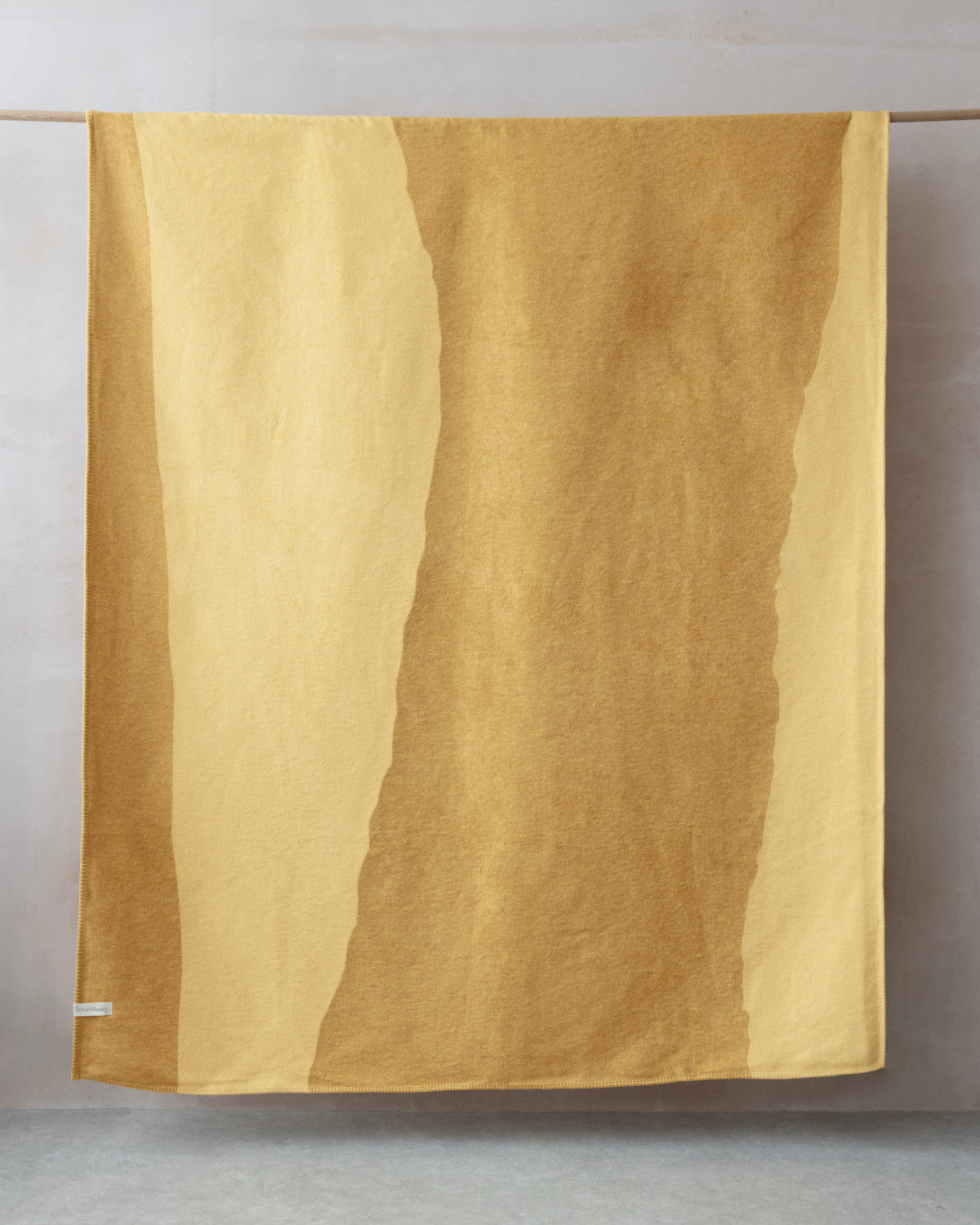 Cloud Cotton Blanket: Tide in Butter, draped on a rod, displays warm yellow ochre tones with organic patterns, woven from recycled cotton with a brushed finish.