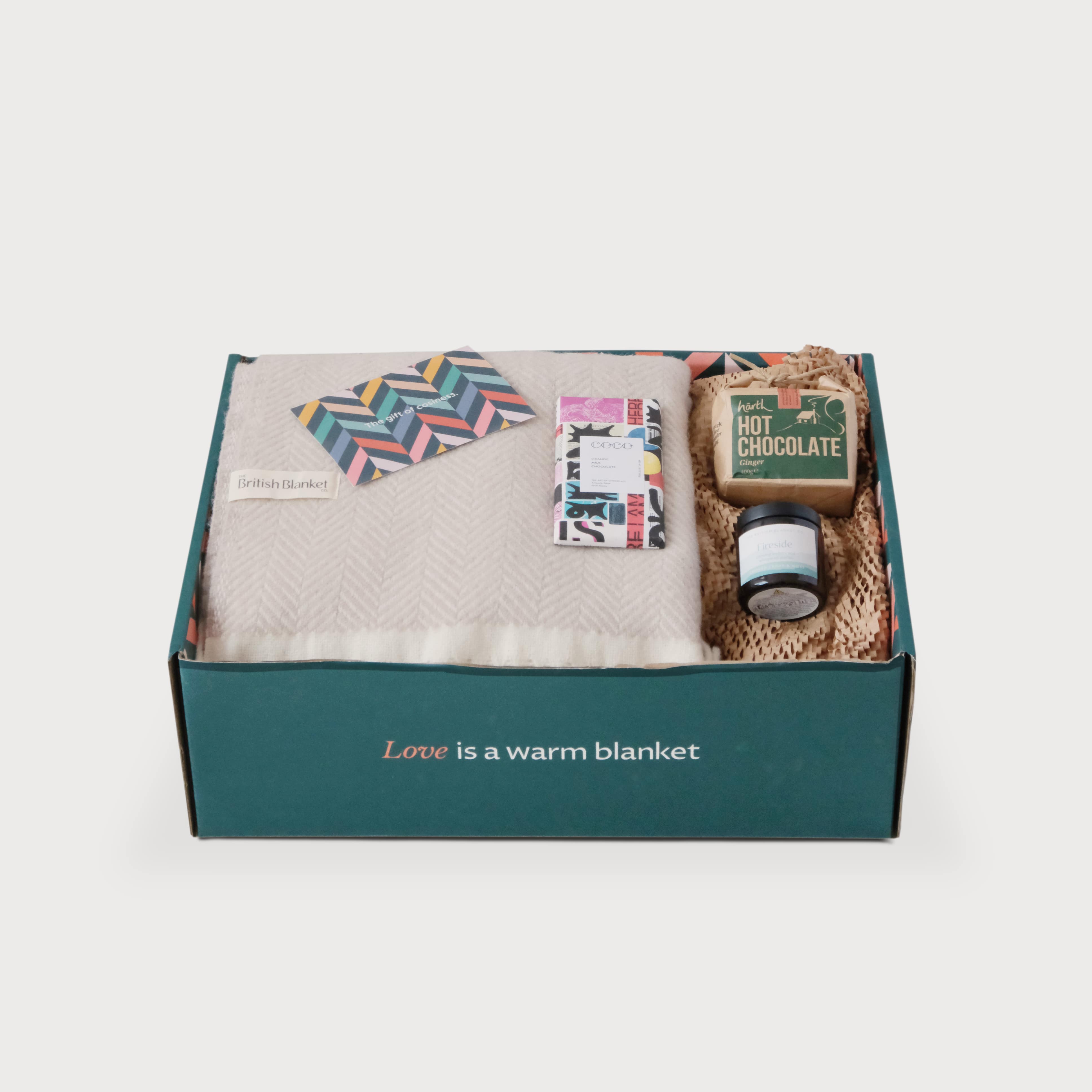 The Christmas Blanket Gift Box: Bath Stone features a British Blanket, greeting card, Coco Co. chocolate, candle, and ginger hot chocolate mix in a teal box.