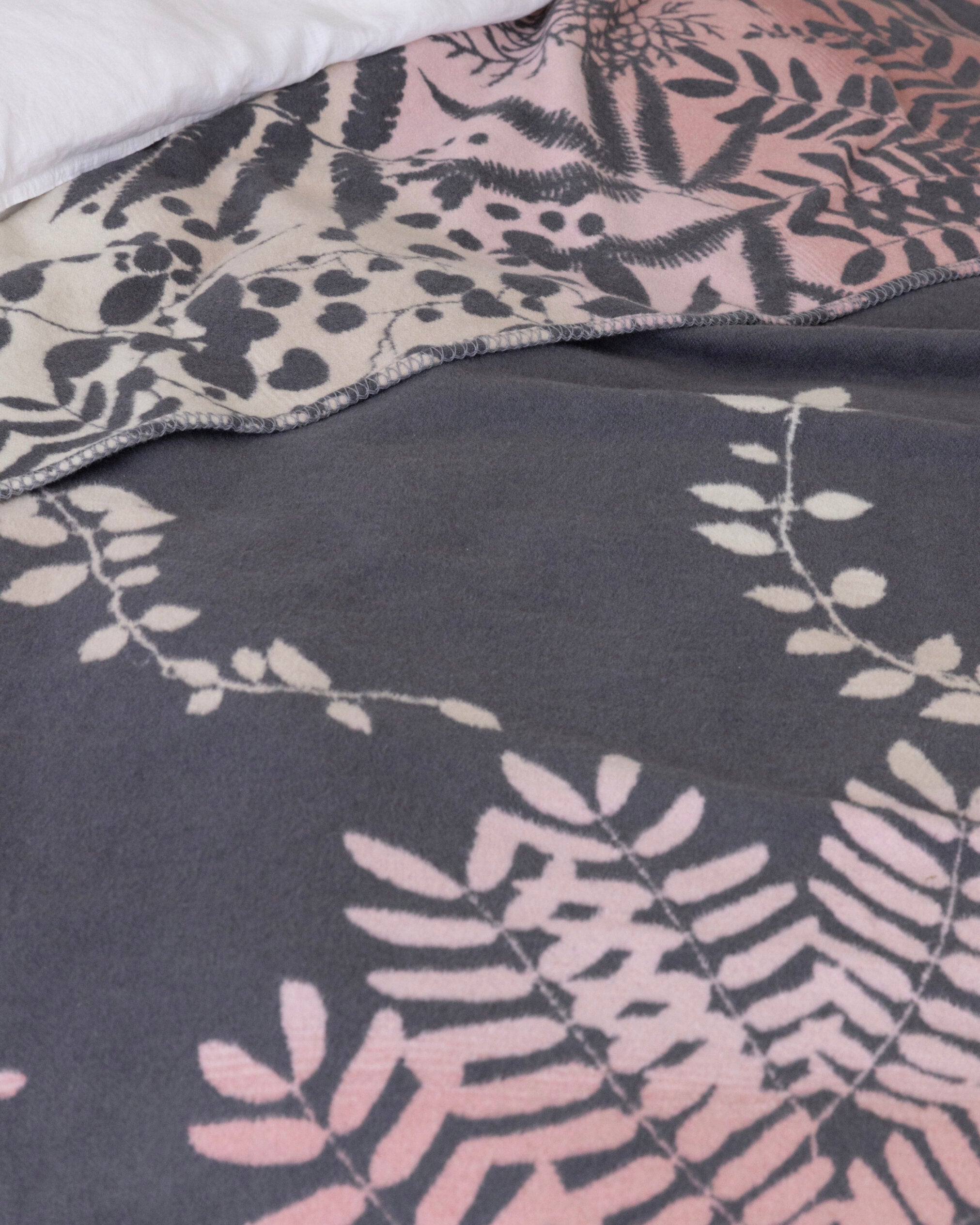 Clarissa Hulse Blanket: Kaleidoscope in Shell, featuring soft fleece with botanical motifs in muted tones on a jacquard-woven, reversible design, partially folded back.