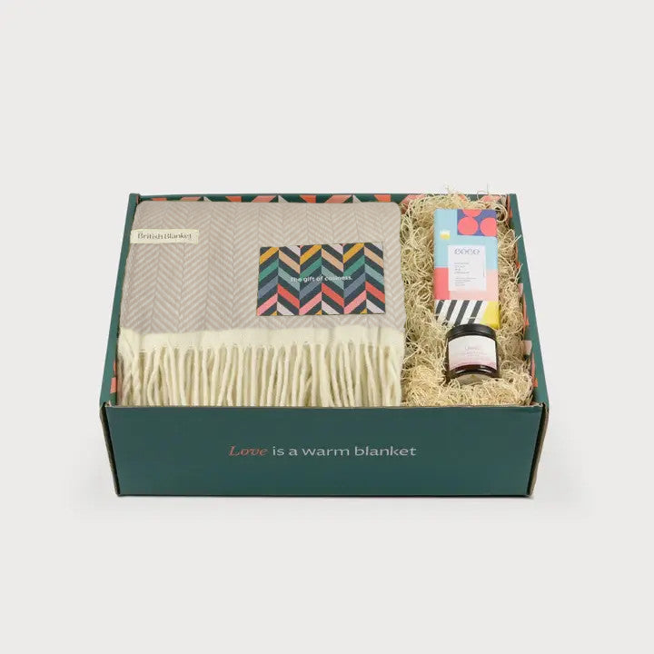 Clifton Blanket Hamper: Bath Stone features a fringed blanket, a colorful bar, and a glass jar, all elegantly packed in a green box.