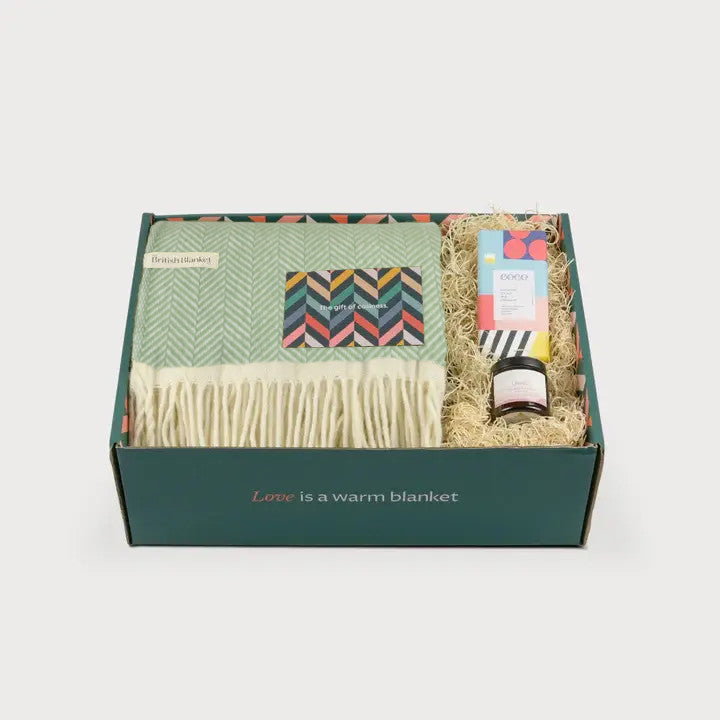 Clifton Blanket Hamper: Birdcage features a pale green herringbone wool blanket, gourmet bar, and a small jar in a forest-green box.