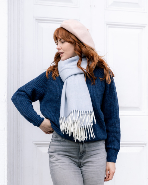 Person wearing an Oversized Blanket Scarf: Smoke, draped stylishly with its soft herringbone weave and ivory tassels, complementing their cozy, cool-weather outfit.