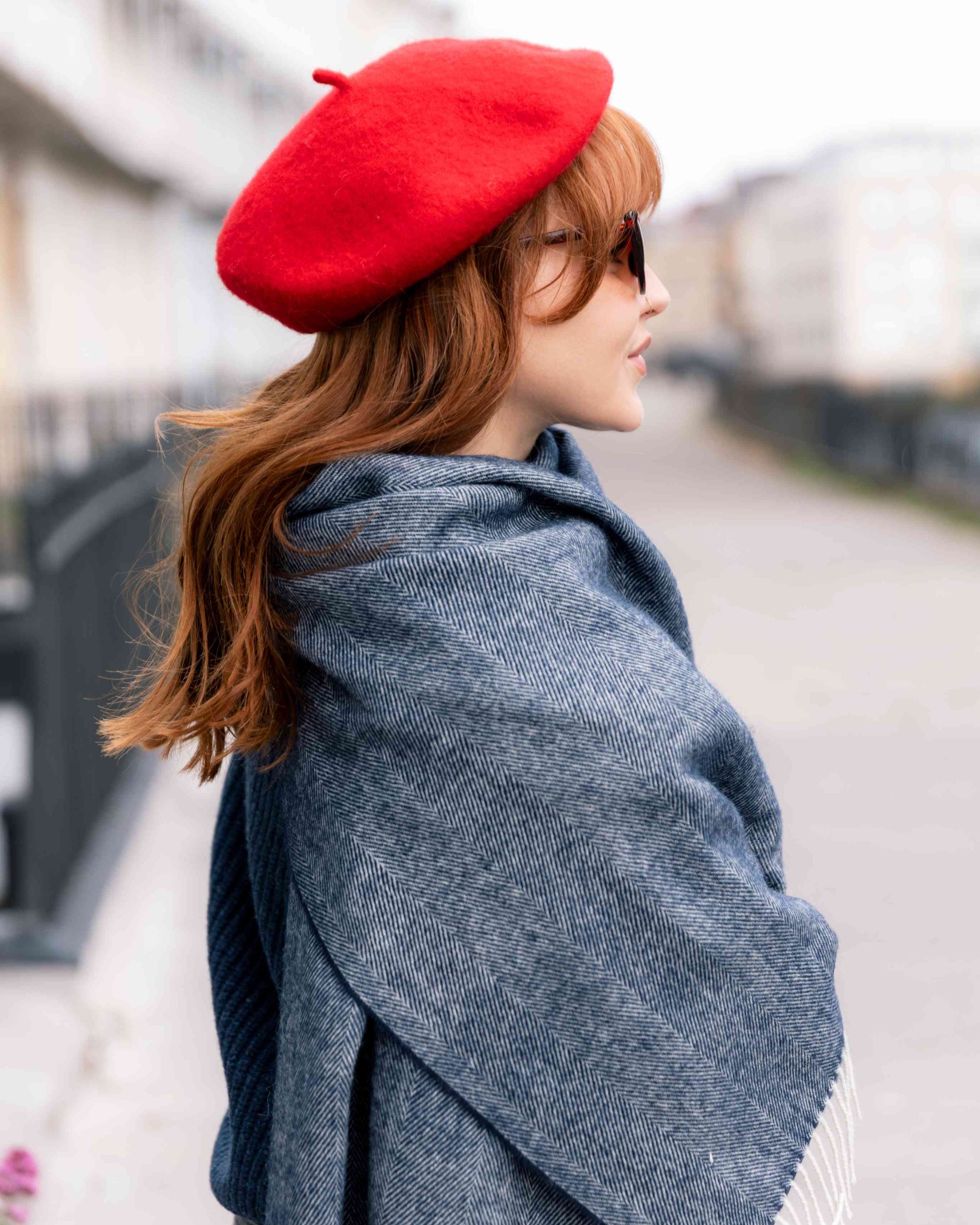 Person in profile wearing a Wool Beret Hat: Red, showcasing its thick, durable design. Paired with a gray-blue herringbone shawl, highlighting stylish warmth.