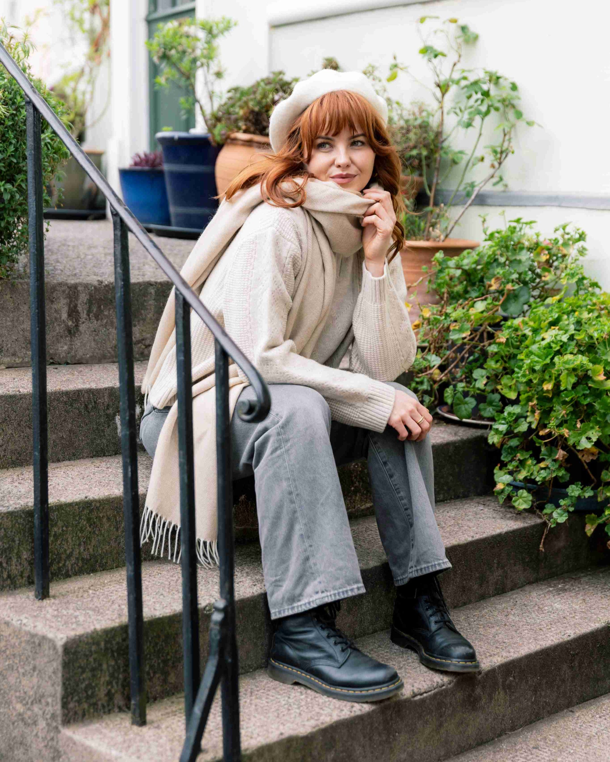 Woman sitting on stoop wearing an Oversized Blanket Scarf: Basswood, with a fringed design, showcasing its versatility as a cozy, stylish accessory.