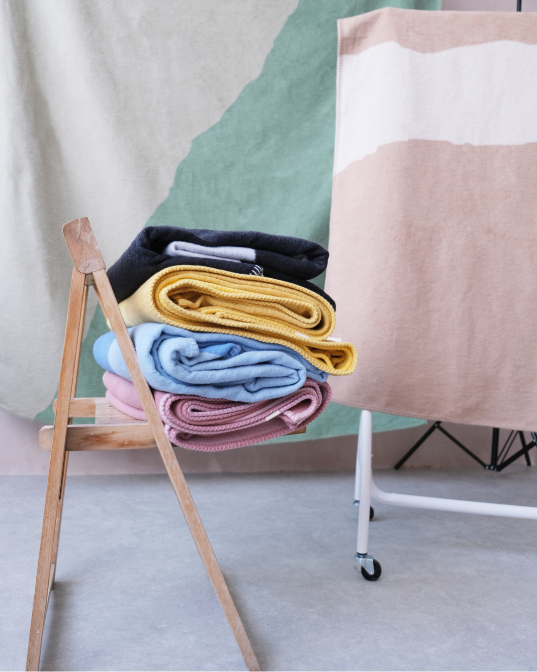 Stack of colourful folded Cloud Cotton blankets on a wooden stand with a neutral background