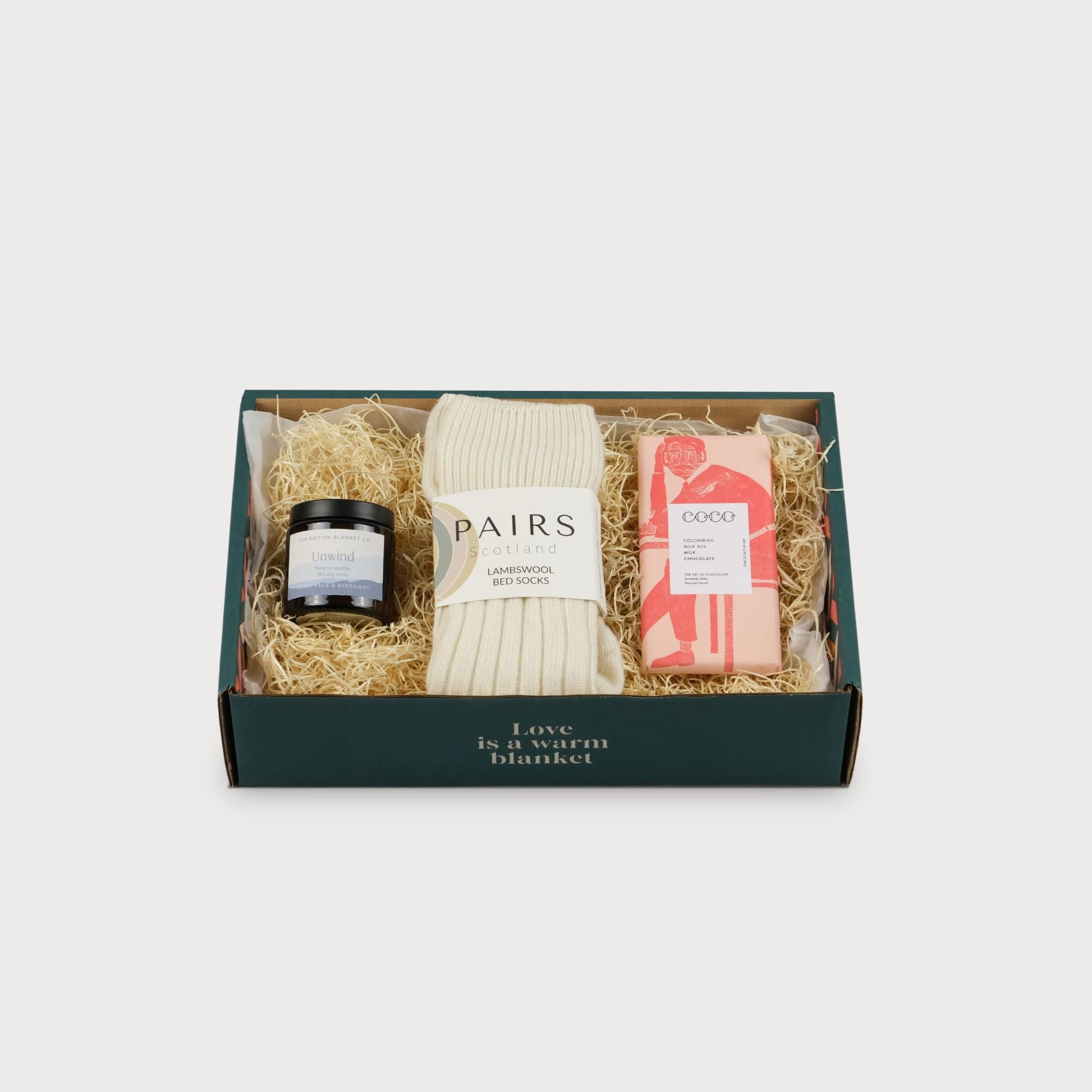 Cosy Gift Box: For Her featuring a chocolate bar, a labeled gift box, and a white knitted fabric, highlighting thoughtful packaging and presentation.