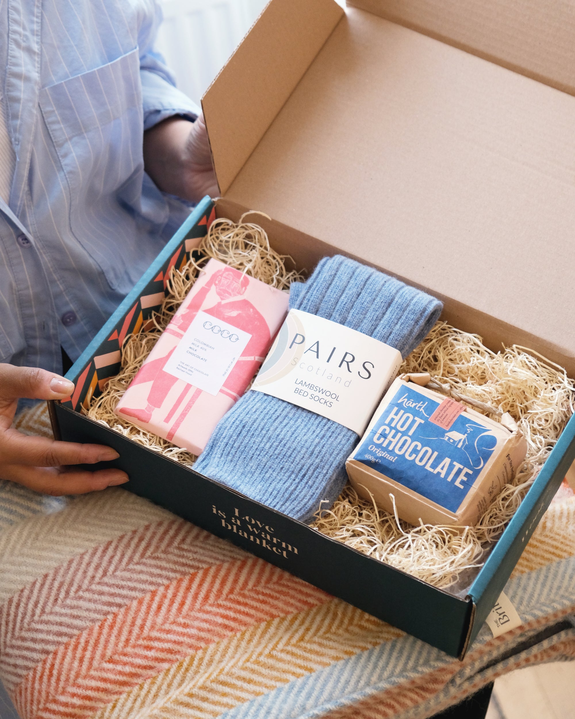 A person presents the Gift Box: Small, ideal for small items like scarves, featuring included tissue paper and a postcard, shown in a hand.