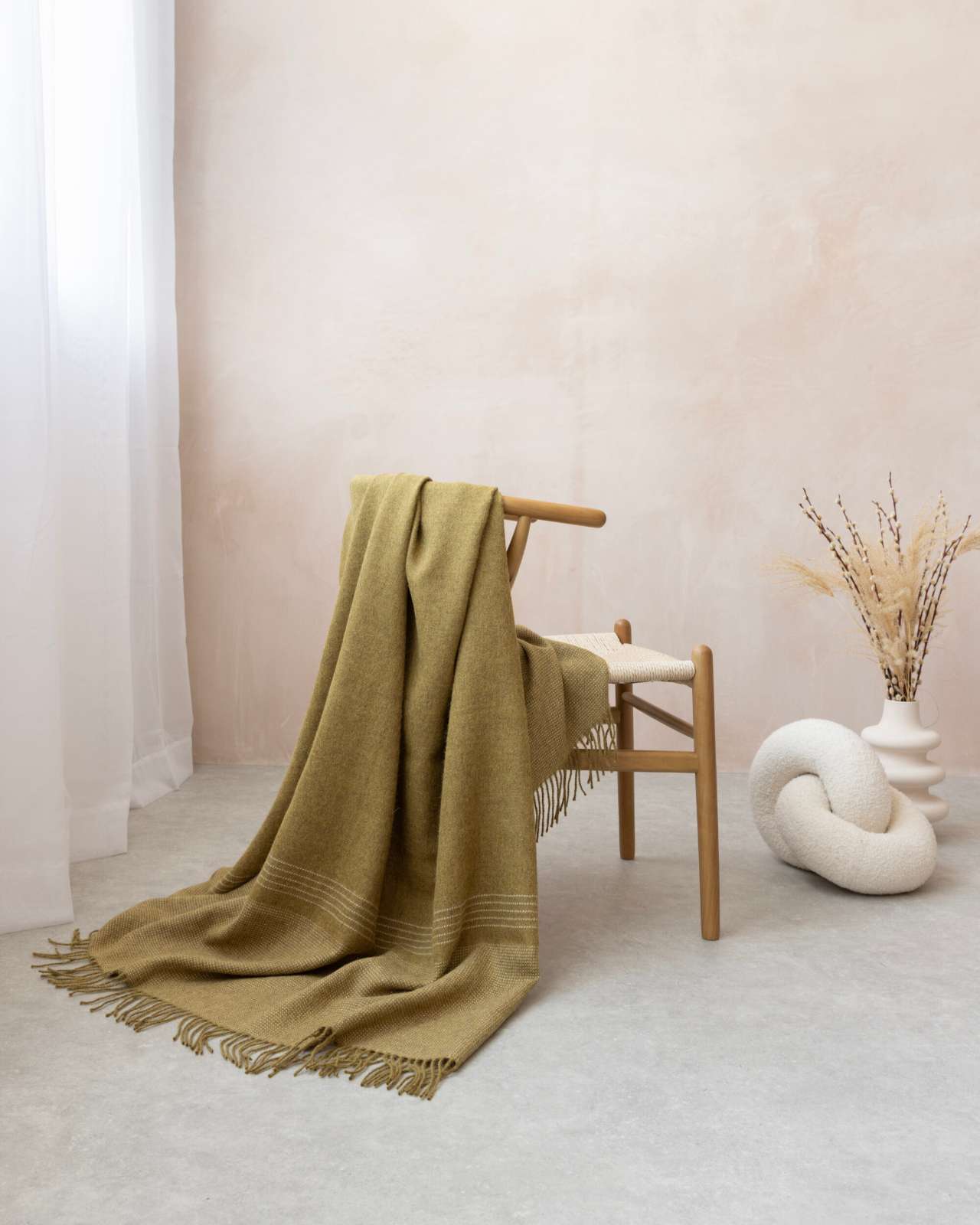 Alpaca Blanket Gift Box: Golden Moss displayed on a wooden bench, featuring an olive-green alpaca blanket with stripe details, complemented by a knot cushion and decorative vase.
