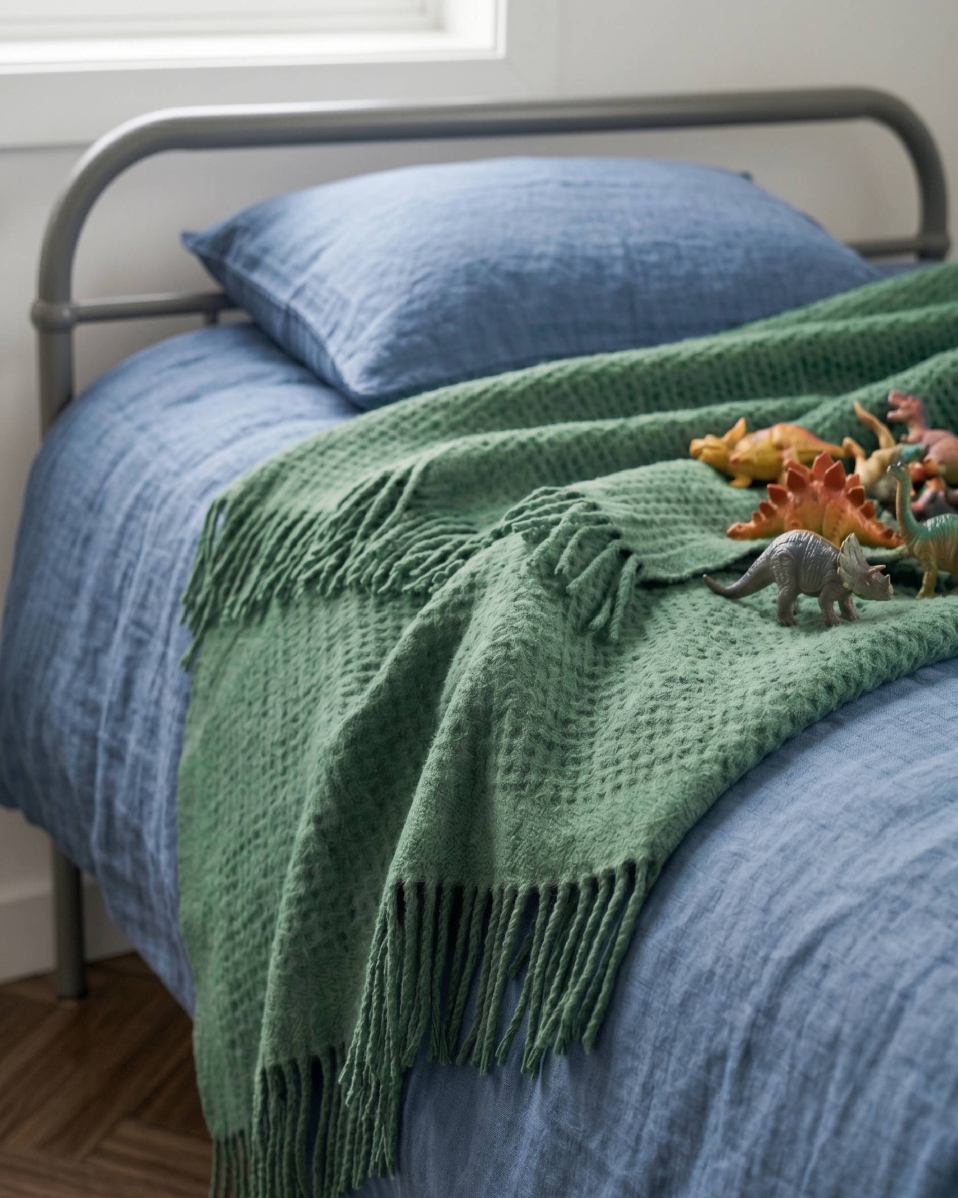 Green Waffle Kids blanket on a childs bed, covered in toy dinosaurs