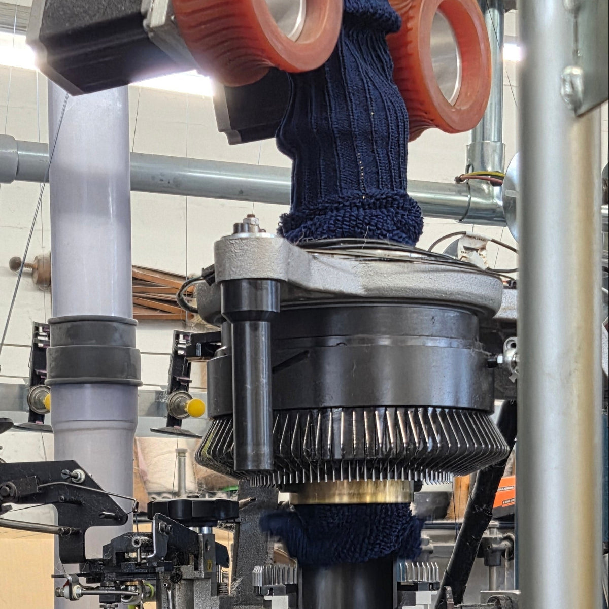 Industrial machinery with metal pipes, transparent glass or plastic vessels, and orange circular components in a factory setting.