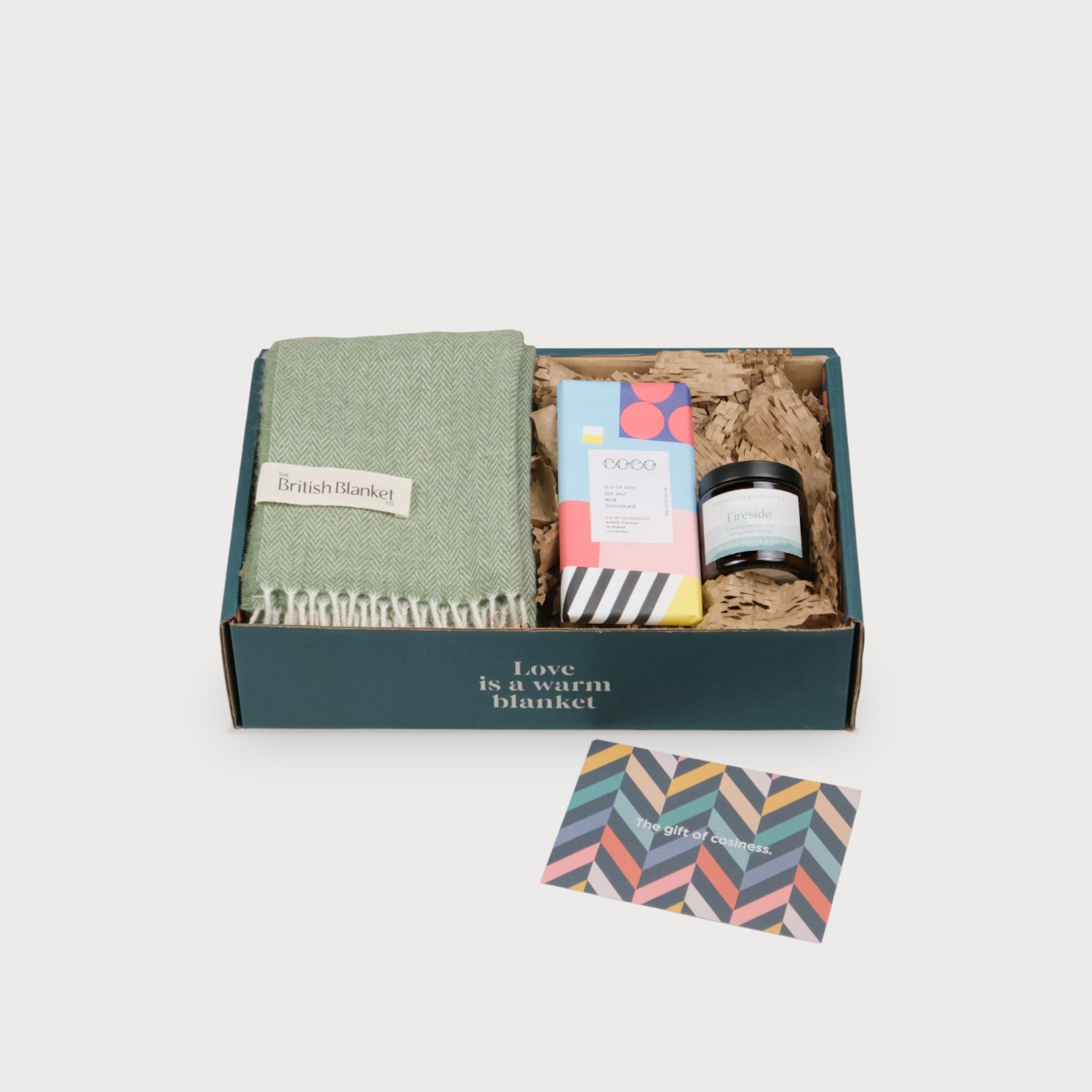 Scarf Gift Box: Apple Herringbone features a green blanket, artisan chocolate, a Fireside candle, and a card, all in a printed gift box.