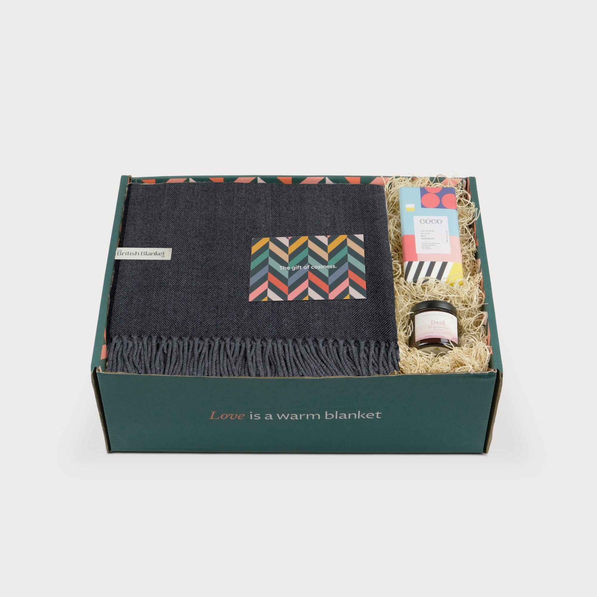 Merino Blanket Gift Box: Graphite Grey with a folded blanket, greeting card, Coco chocolate, and candle in a green box.