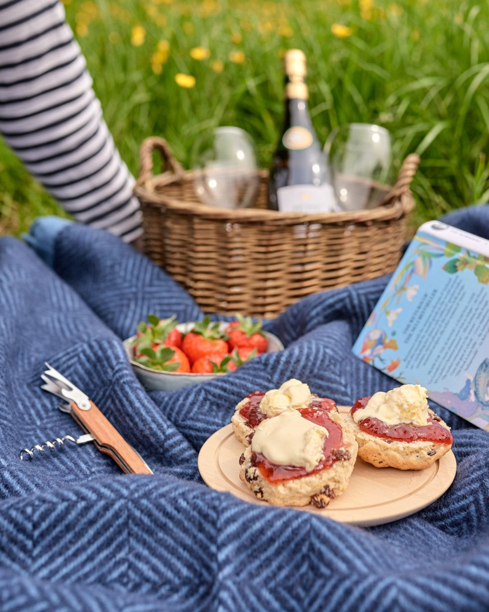 Blue wool picnic blanket rolled up with picnic food, cream tea and drinks