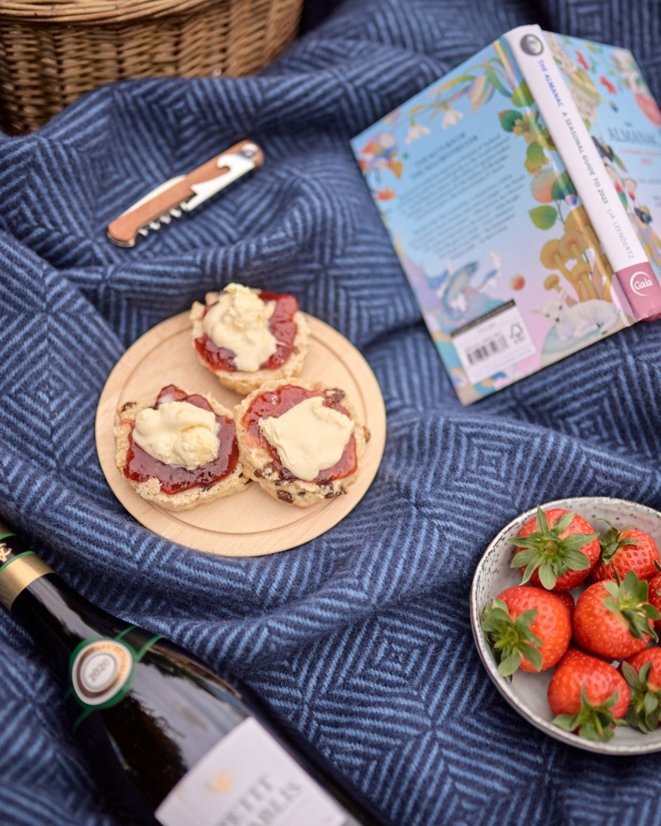 Blue wool picnic blanket rolled up with picnic food, cream tea and drinks