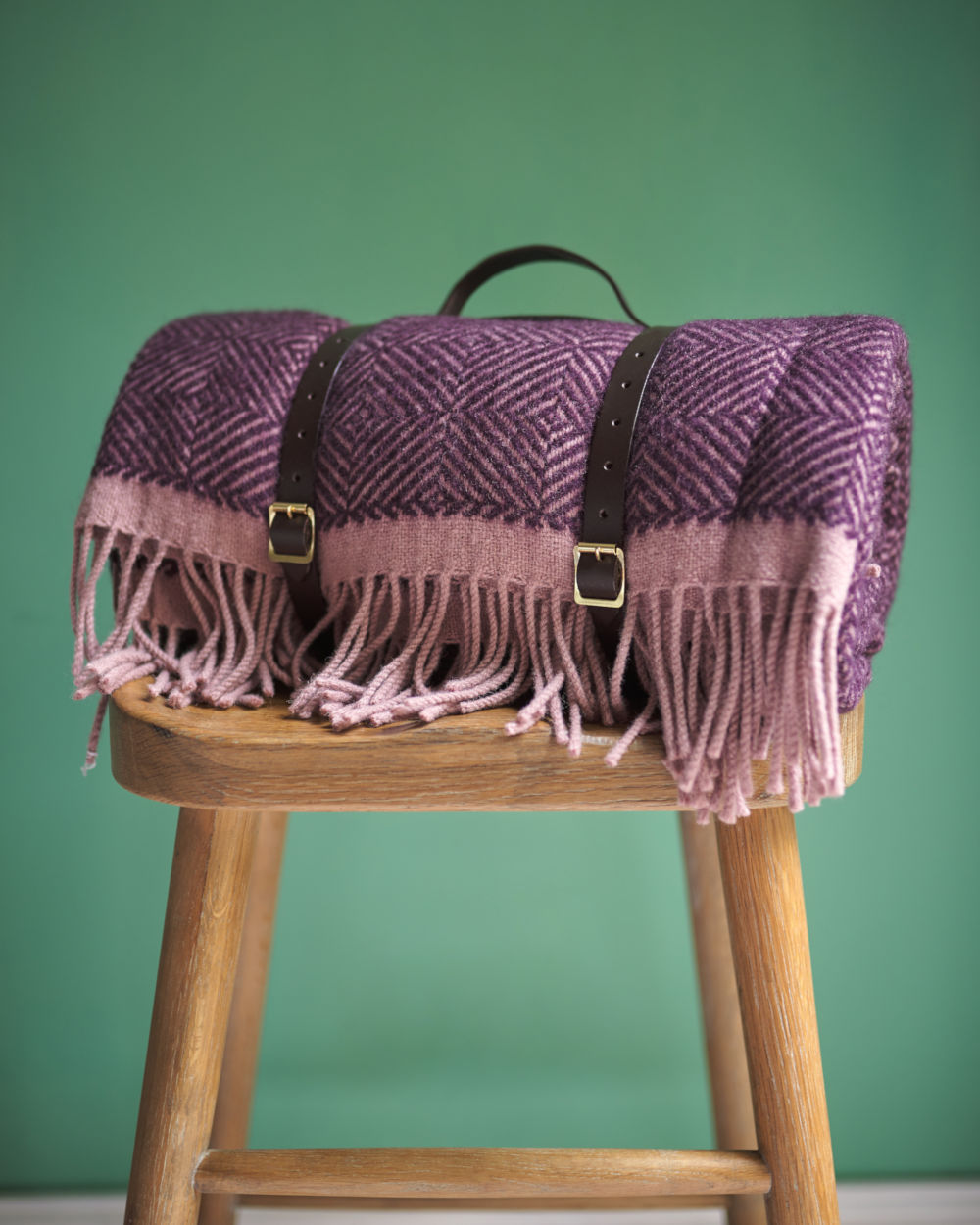 Purple wool picnic blanket with leather straps on stool from The British Blanket Company