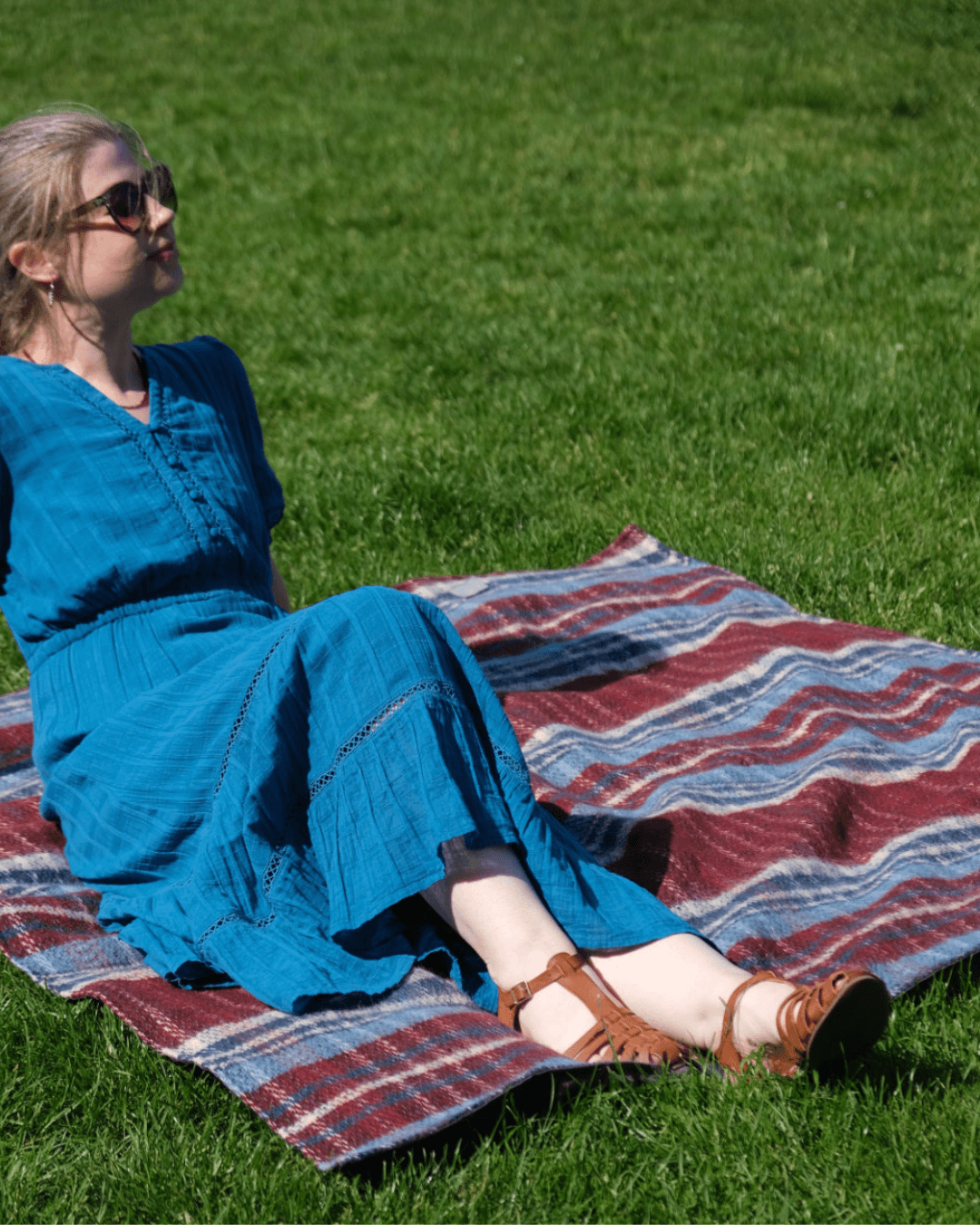 Woman in a blue dress sitting on a waterproof-back Random Recycled Picnic Blanket in a grassy field