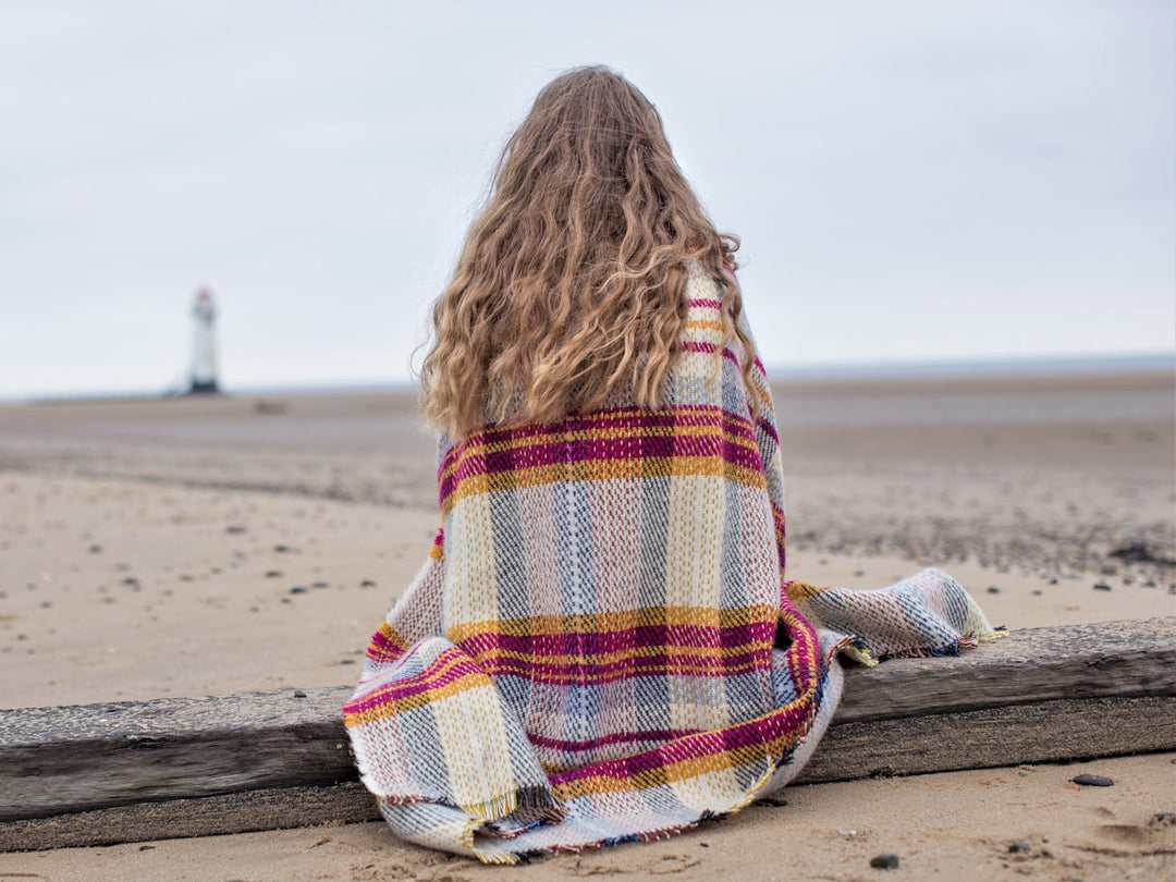 woman sitting on a beach wrapped in Random recycled wool throw blanket - The British Blanket Company