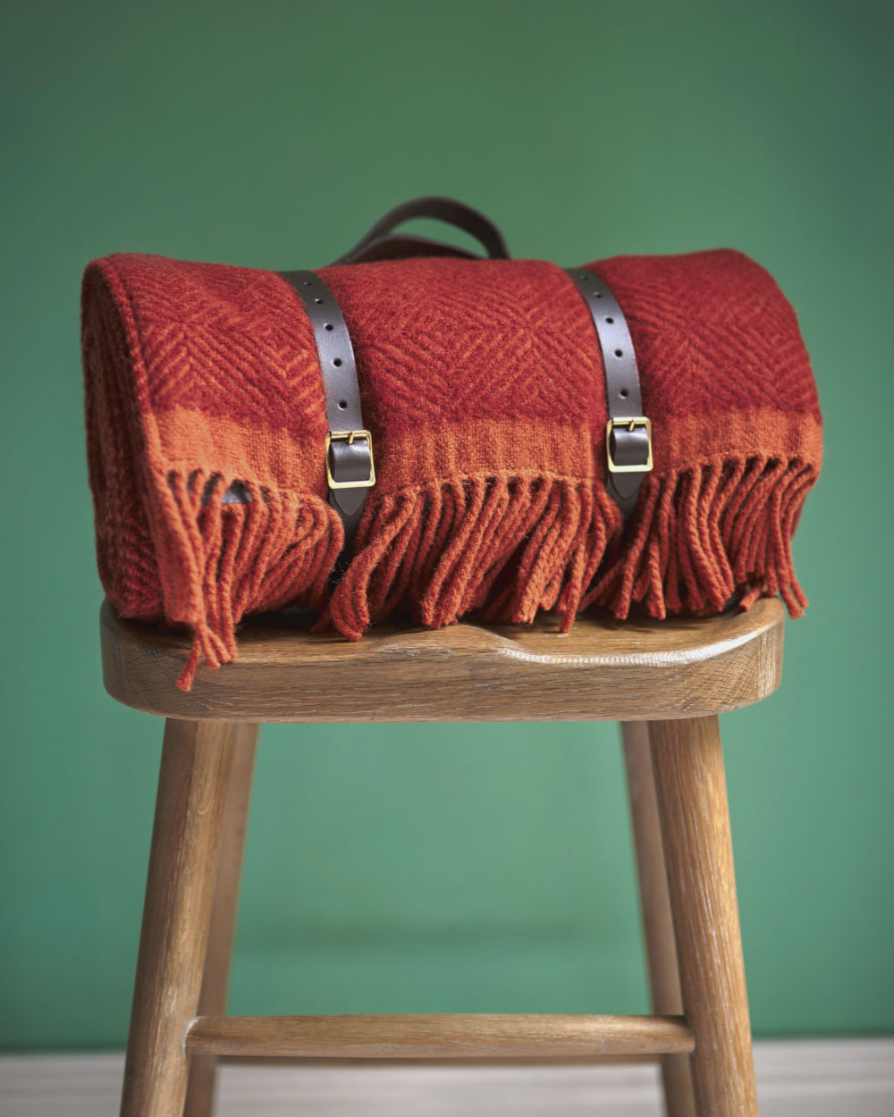Red wool picnic blanket with leather straps on stool from The British Blanket Company
