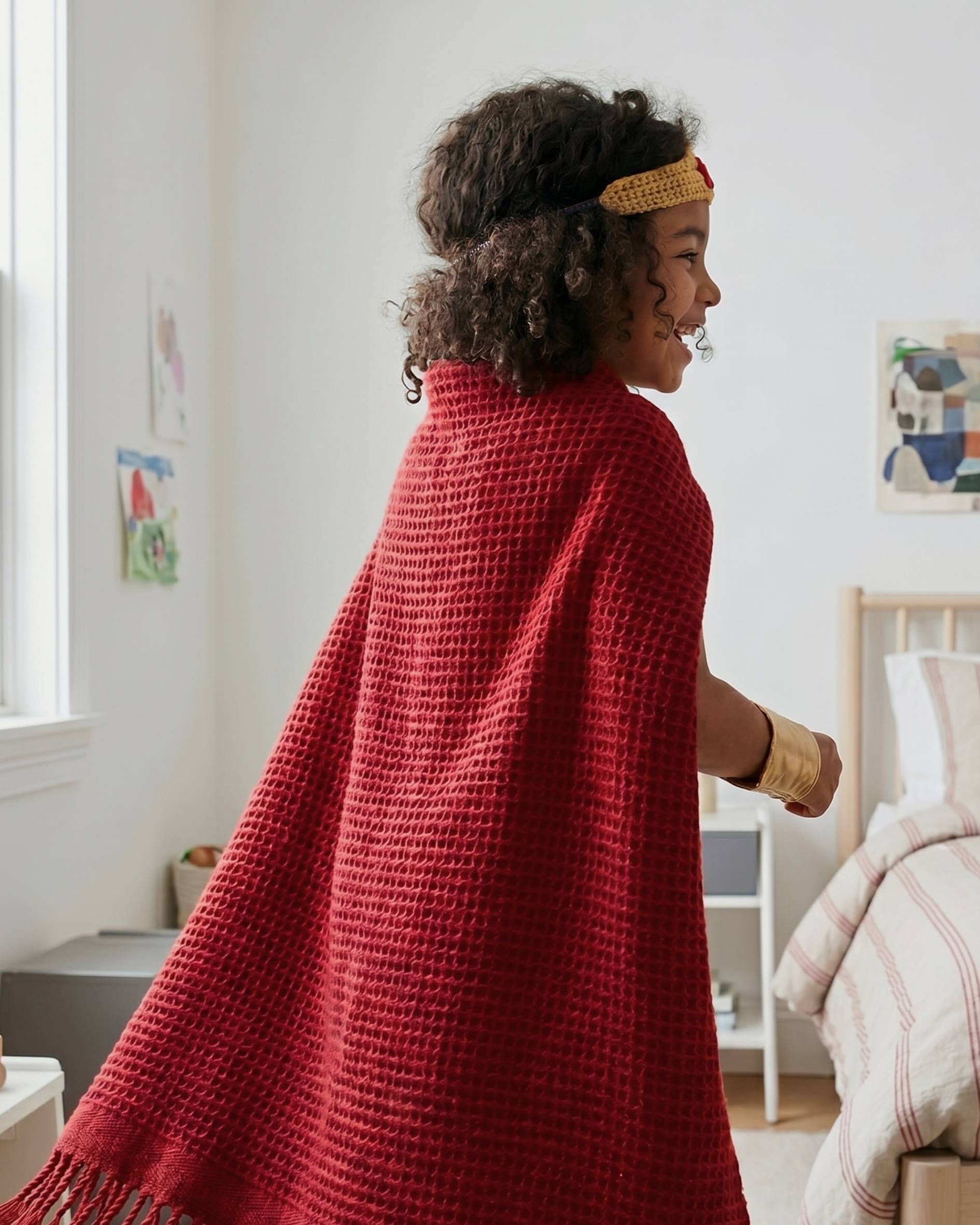 Young Girl playing superhero in her bedroom, with a Red waffle kids blanket from the British Blanket Company