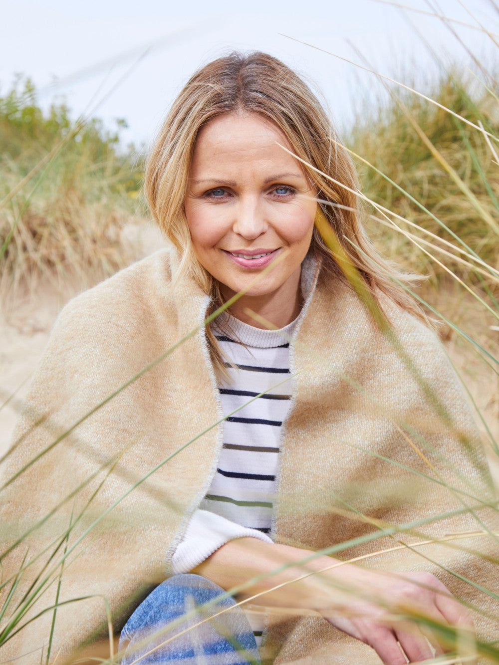 woman on a beach wrapped in a sand wool blanket from the british blanket company