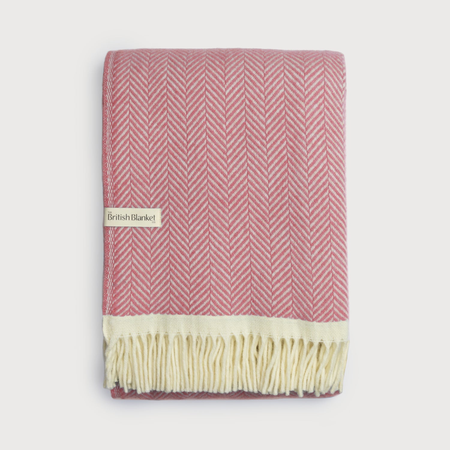 Clifton Blanket Gift Box: Rose features a folded pink-and-off-white herringbone wool blanket with a cream fringe, showcasing The British Blanket Co. label against a light background.