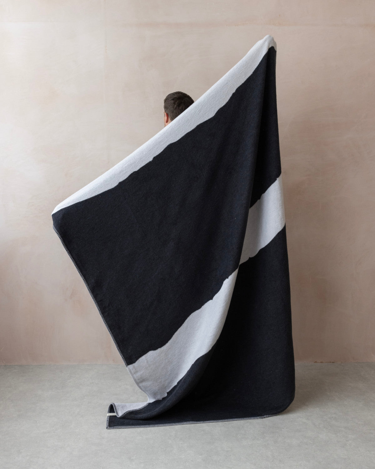 Person holding the Cloud Cotton Blanket: Strata in Flint, featuring a black body with a wide light-gray stripe, woven from recycled cotton with a soft finish.