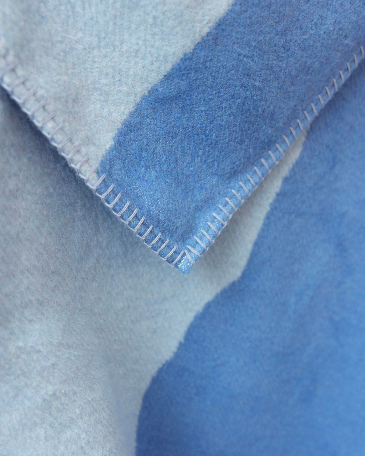 Cloud Cotton Blanket: Tide in Cornflower, featuring a soft, brushed-wool texture, two-tone blue hues, and contrasting whip-stitch edges, crafted from eco-friendly recycled cotton.