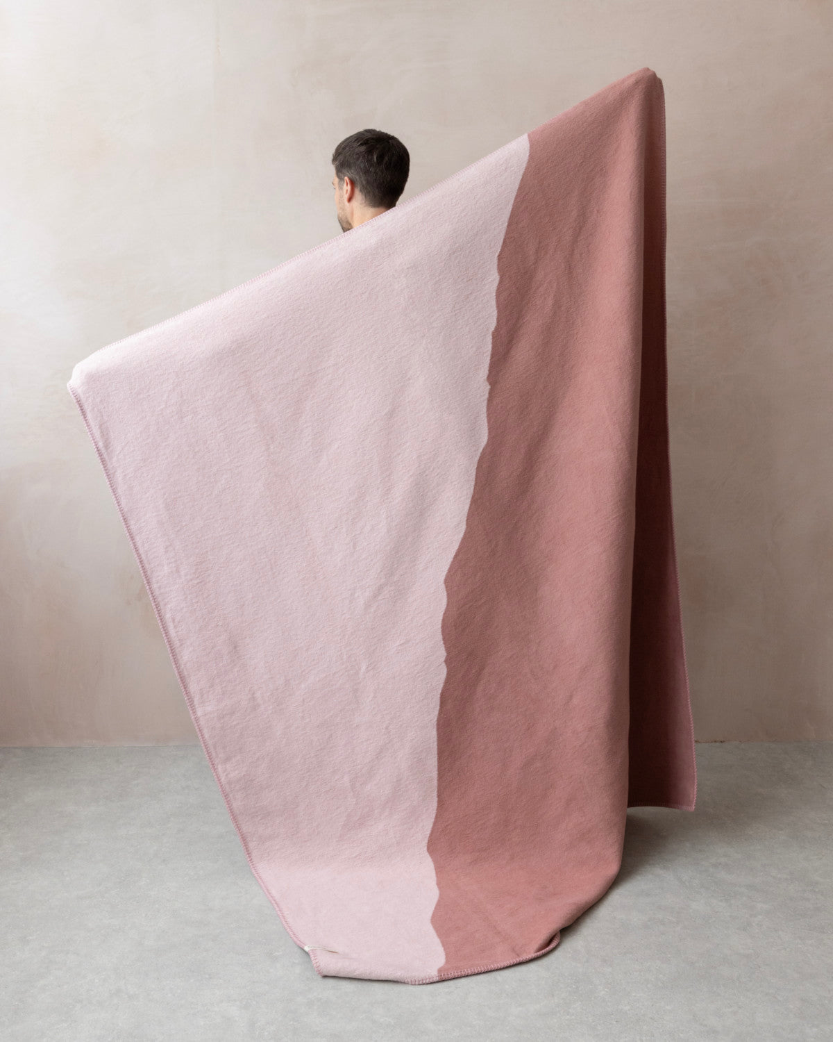 Person holds Cloud Cotton Blanket: Vale in Blush, showcasing its two-tone pink design with organic lines, crafted from recycled cotton for a fleece-like feel.