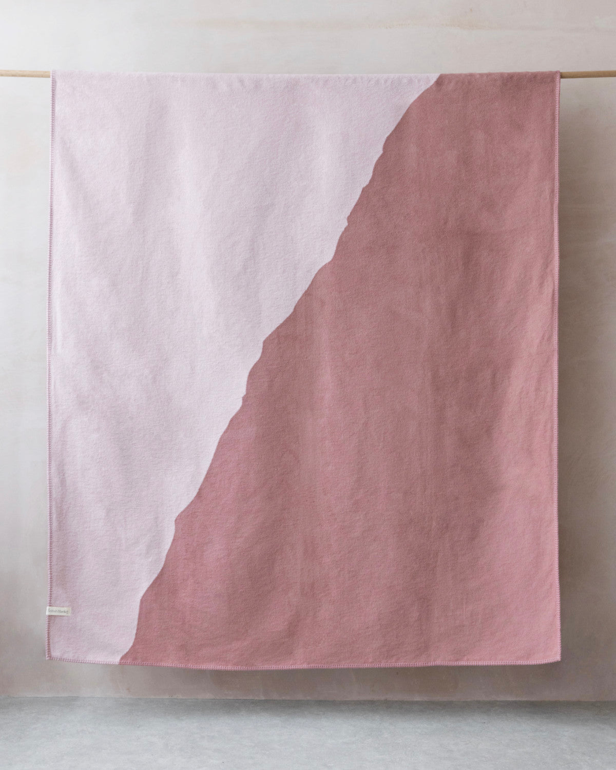 Cloud Cotton Blanket: Vale in Blush draped over wooden rod, showcasing its soft, brushed texture and hand-stitched edge in two-tone blush and dusty rose.