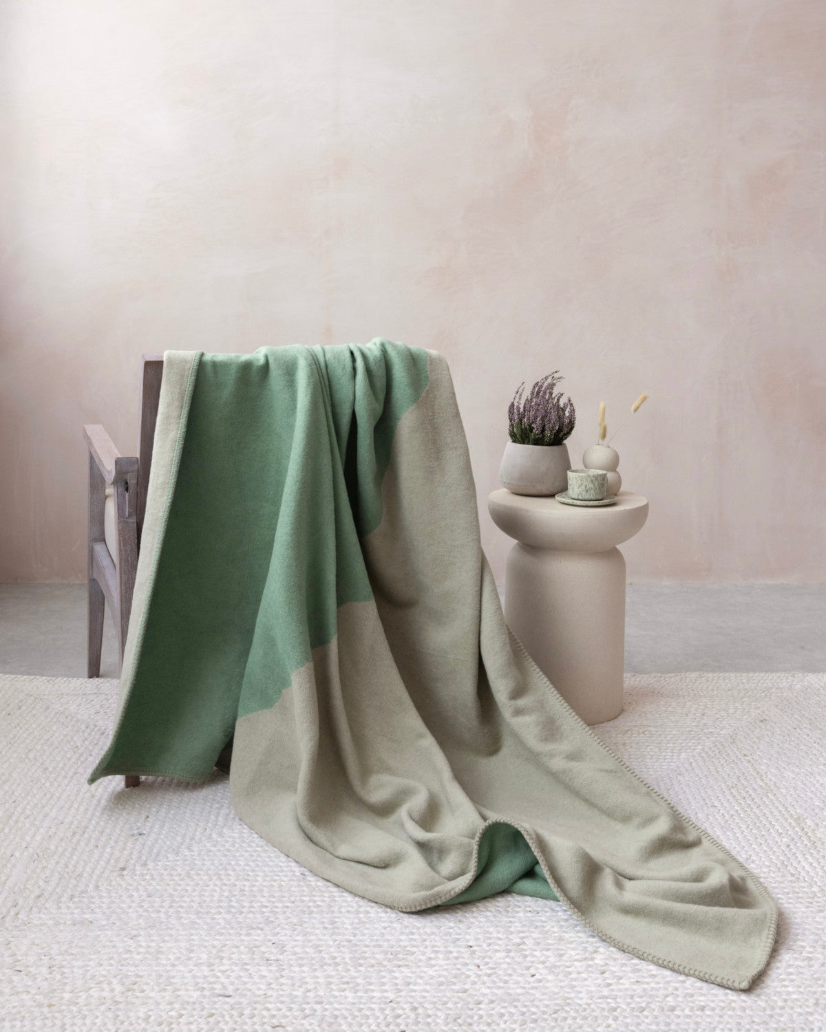 Cloud Cotton Blanket: Vale in Thyme draped on a wooden armchair, showcasing its two-tone design, with a soft, brushed finish and blanket-stitched edge.
