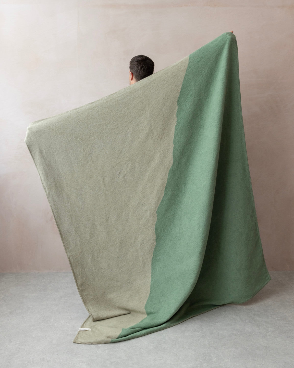 Person draped in Cloud Cotton Blanket: Vale in Thyme, showcasing a two-tone design with fleece-like texture, woven from recycled cotton.