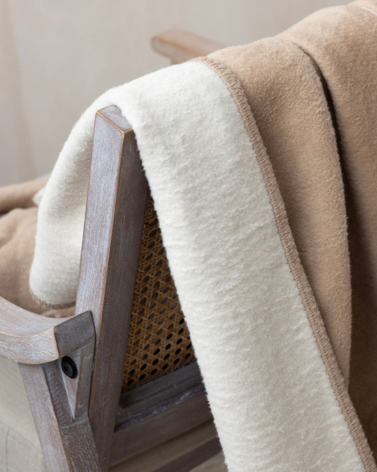 The Cloud Cotton Blanket: Strata in Clay, woven from recycled cotton, drapes over a wooden chair showcasing its two-tone design and fleece-like texture.