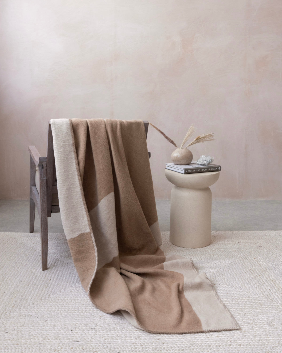 Cloud Cotton Blanket: Strata in Clay drapes over a rustic armchair, showcasing its two-tone design and plush texture, complemented by a ceramic side table with decor.